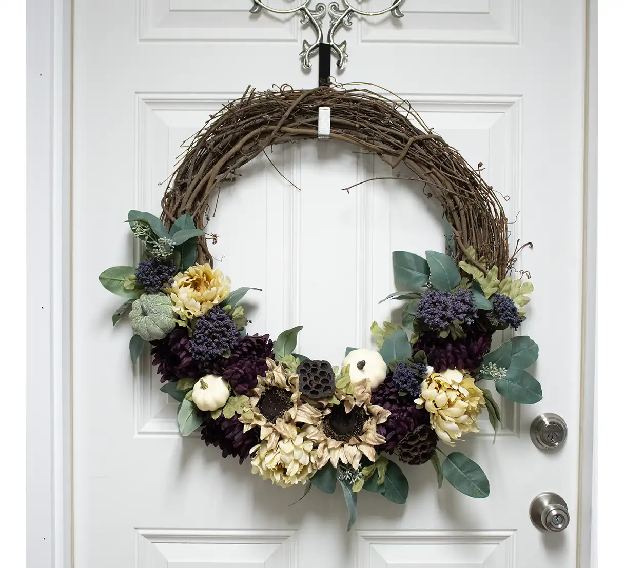 Accents of faux berries in warm copper and dusty purple hues are artfully scattered, while natural-looking pinecones provide a rustic finishing touch. The grapevine base peeks through, grounding the design with its natural texture. A cascading ribbon in deep plum or burlap adds a polished yet understated elegance. Perfect for adorning a front door or interior wall, this wreath captures the essence of autumn’s cozy charm. Durable and timeless, it’s a celebration of fall’s bounty, bringing seasonal warmth to any space.